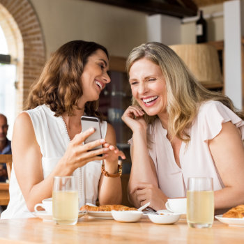 Two women laughing and enjoying a conversation over breakfast at a cafe.