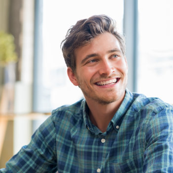Smiling young man in a plaid shirt looking away from the camera.
