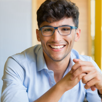 A smiling young man with glasses wearing a light blue shirt.
