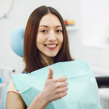 A smiling woman giving a thumbs up while sitting in a dental chair.