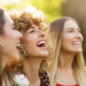 Three women smiling outdoors in the sunlight.