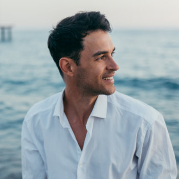 Man smiling while looking away against a seascape background.