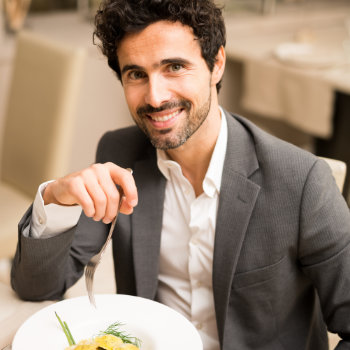 A smiling man in a suit holding a fork over a plate of food in a restaurant.