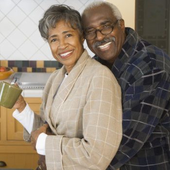 Mature couple smiling and embracing in a kitchen setting.