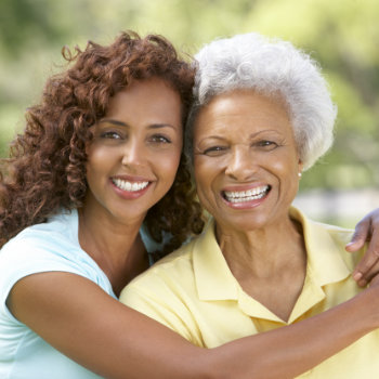 Two smiling women outdoors, possibly representing a mother and daughter, embracing and looking at the camera.