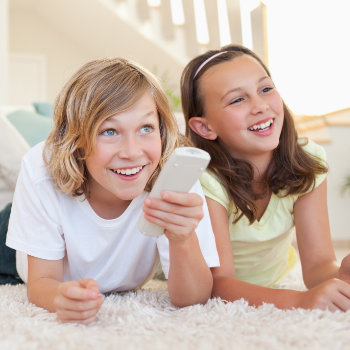 Two children lying on the floor smiling and looking at a smartphone.