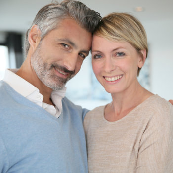 A smiling middle-aged couple posing closely and looking at the camera.