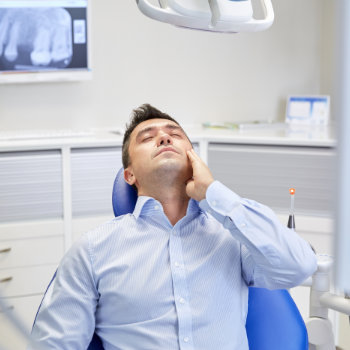 Man experiencing discomfort in dental chair, possibly waiting for a dentist.