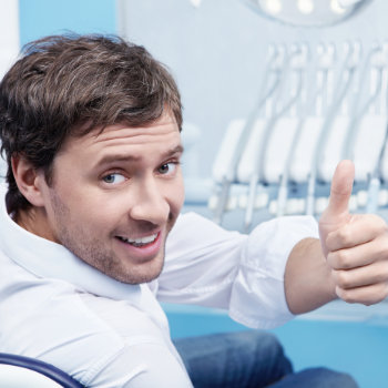 Man giving a thumbs up while sitting in a dentist's chair.