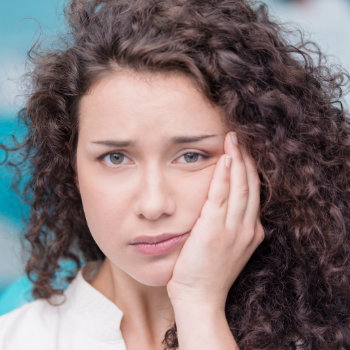 Woman with curly hair looking worried or distressed, holding her cheek.