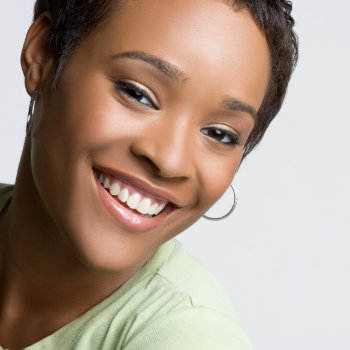 A smiling woman with short hair and hoop earrings against a grey background.