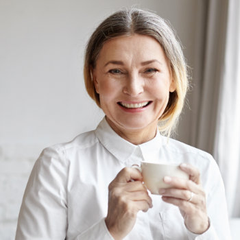 A smiling woman in a white shirt holding a coffee cup.