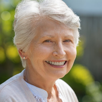Elderly woman smiling outdoors on a sunny day.
