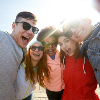 Group of cheerful friends taking a selfie in bright sunlight.