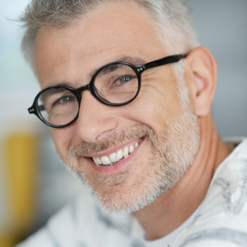 A portrait of a smiling middle-aged man with salt-and-pepper hair wearing black-rimmed glasses.