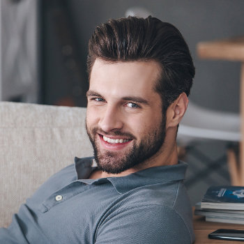 A smiling man with a beard sitting indoors.