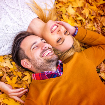 A couple lying on autumn leaves, smiling joyfully.