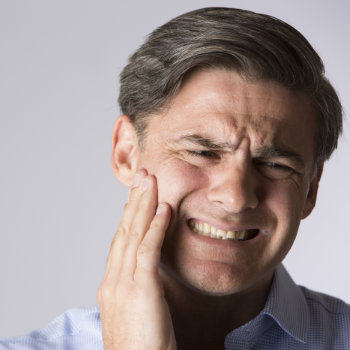 Man grimacing and holding his cheek, possibly experiencing dental pain.