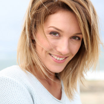 A smiling woman with short blond hair wearing a white knit sweater.