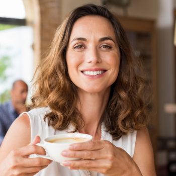 A smiling woman holding a cup of coffee in a cafe setting.