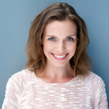 Woman with a bright smile wearing a light pink sweater against a blue background.
