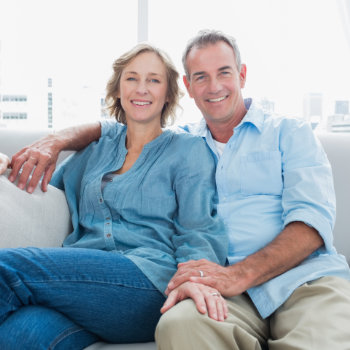 A smiling middle-aged couple sitting closely together on a sofa.