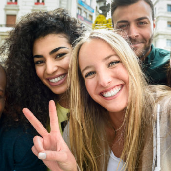A group of cheerful friends posing for a selfie with one person making a peace sign.