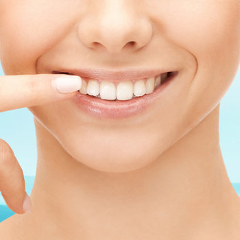 Close-up of a smiling person pointing at their teeth.