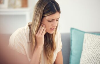 Living room, sofa and woman with mouth in pain for dental inflammation, problem or discomfort of cavity. Home, frustrated and person with sensitive tooth for wisdom teeth, emergency or oral infection